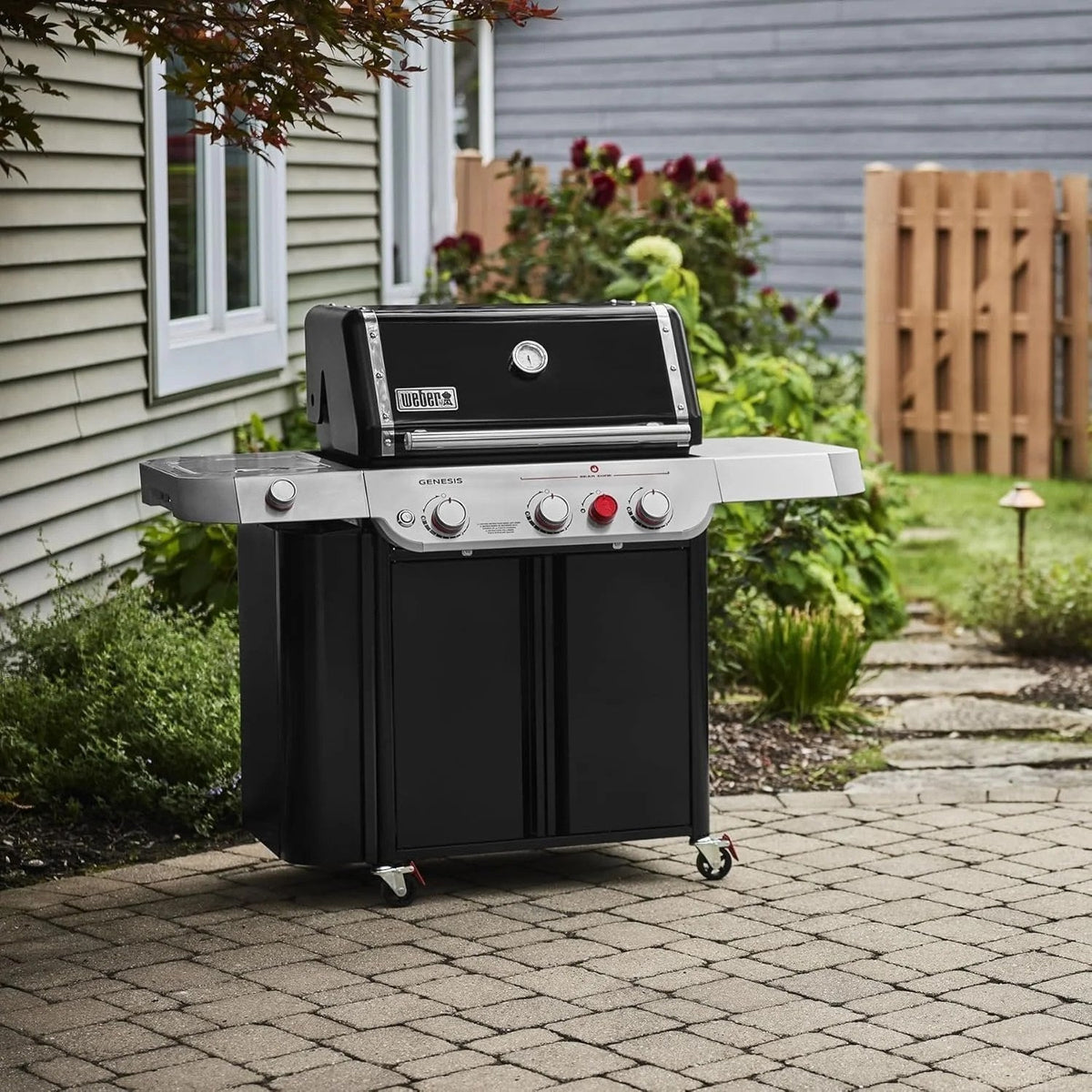 Casavibeo Genesis II E-335 gas grill with four burners, stainless steel lid, side shelves, and cooking grates on a patio.