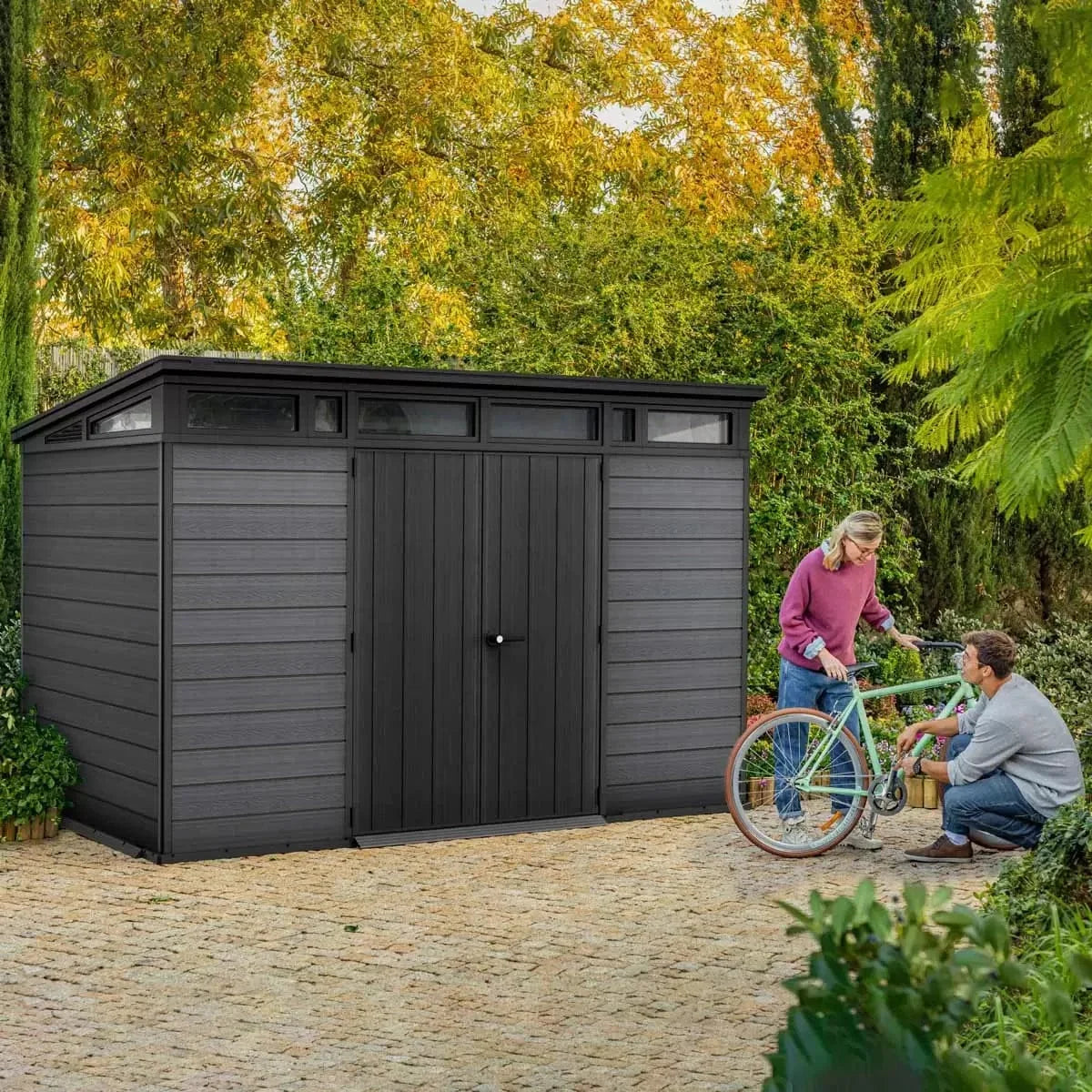 Dark grey Keter Artisan 11x7 ft. outdoor storage shed with floor and window, featuring a modern design and durable construction.