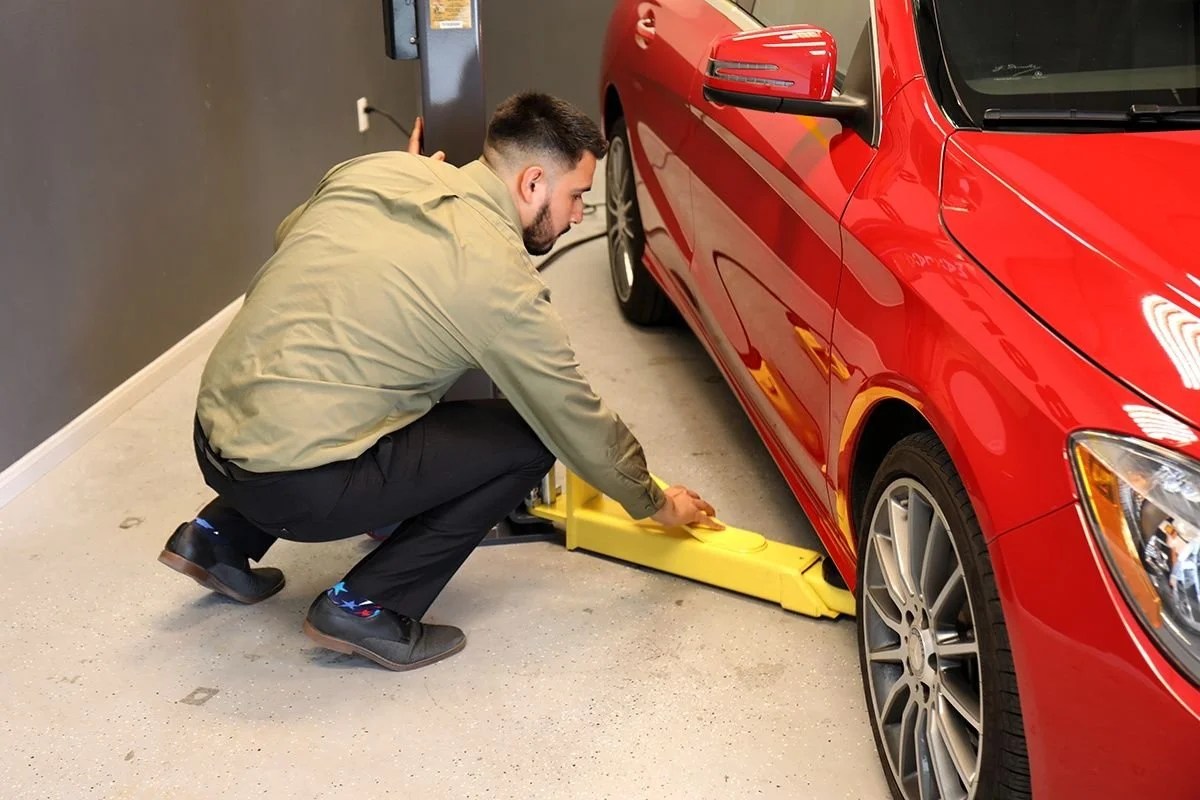 Casavibeo MaxJax portable two-post garage lift with metal arms and hydraulic system for vehicle lifting in a garage setting.