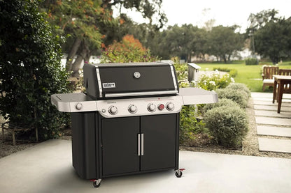Casavibeo Weber Genesis E-435 gas grill with four burners, stainless steel lid, side shelves, and control knobs in a backyard setting.