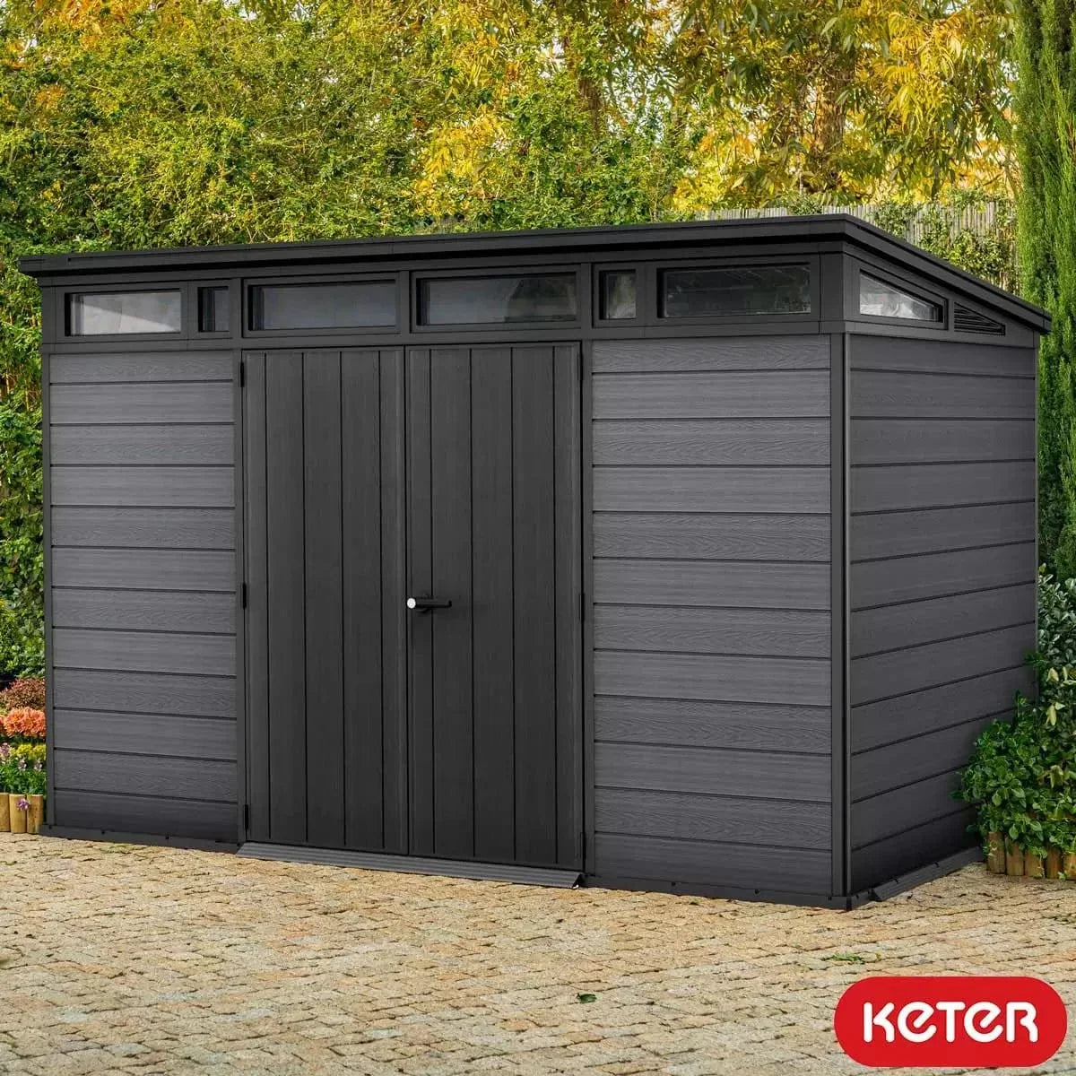 Dark grey Keter Artisan 11x7 ft. outdoor storage shed with floor and window, featuring a sturdy design and ample storage space.