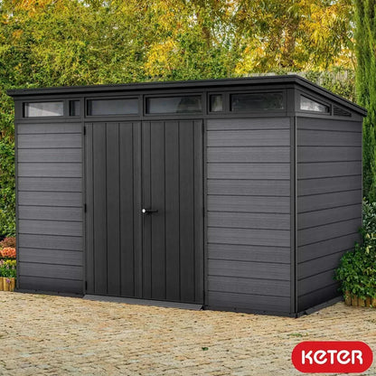 Dark grey Keter Artisan 11x7 ft. outdoor storage shed with floor and window, featuring a sturdy design and ample storage space.