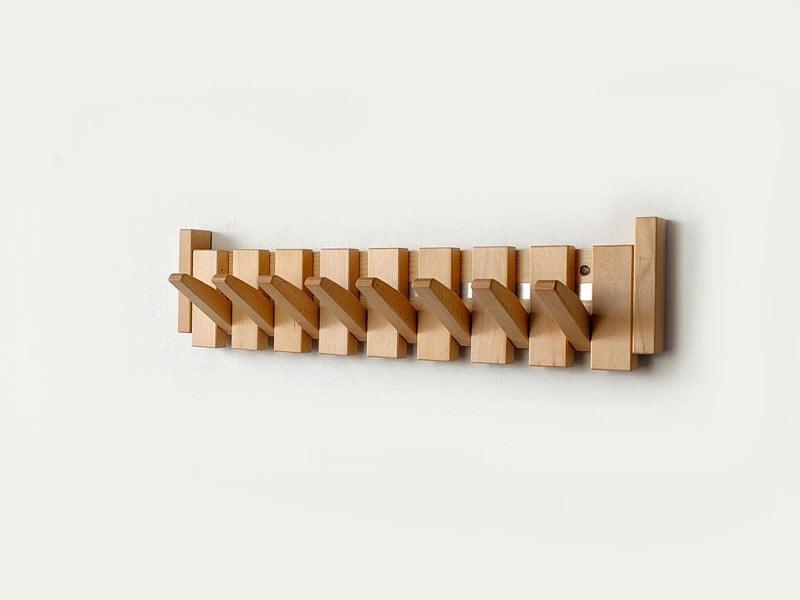 Handmade wooden coat rack by Belro with multiple hooks for jackets and coats, mounted on a wall in a modern entryway.