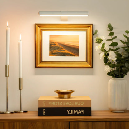 Wireless LED picture light by Belro mounted on a wall, illuminating a framed artwork outdoors in a garden setting.